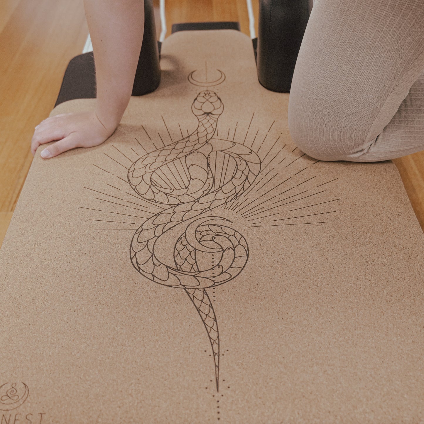 Woman kneeling on moon serpent cork and natural rubber Pilates reformer mat.