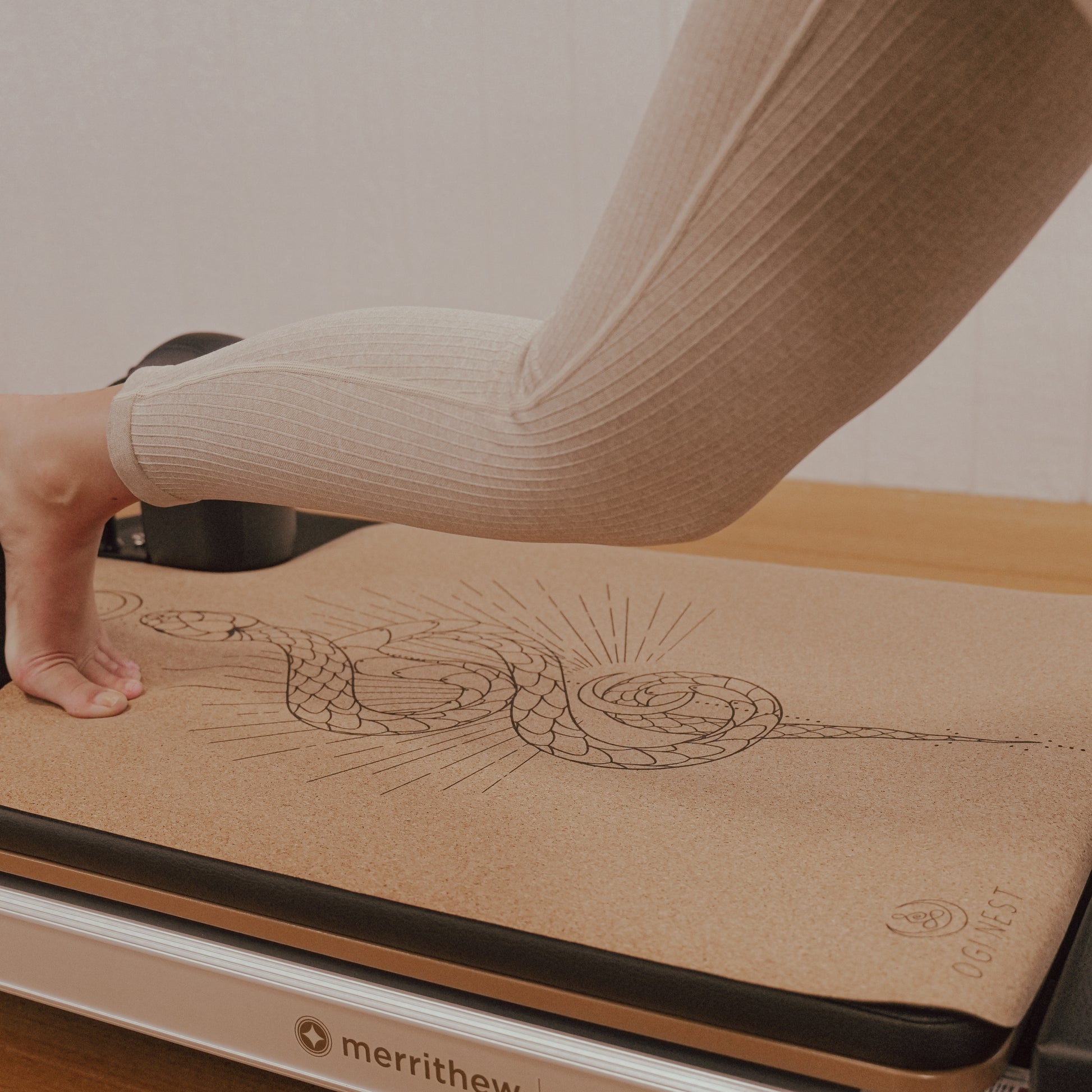 Woman performing single leg push back on moon serpent cork and natural rubber Pilates reformer mat.